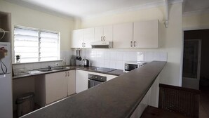 A kitchen with white cabinets, a stainless steel countertop, a window with blinds, and a dishwasher. - Cairns City Garden Apartment (Parramatta Park)