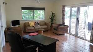 A living room with a sofa, armchair, TV, and a table. - Cairns City Garden Apartment (Parramatta Park)