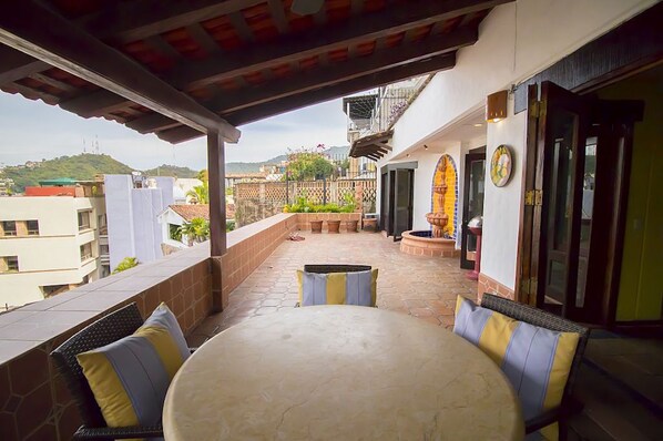 Un patio cubierto con una mesa redonda y sillas, vista a la ciudad y una pared decorada con azulejos.