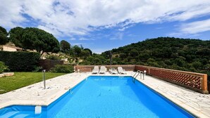 Una piscina rectangular con agua azul cristalina, rodeada por un solárium con baldosas y una valla de madera.