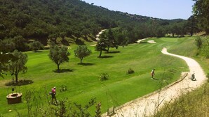 Un campo de golf con un sendero de tierra, árboles y cielo despejado.