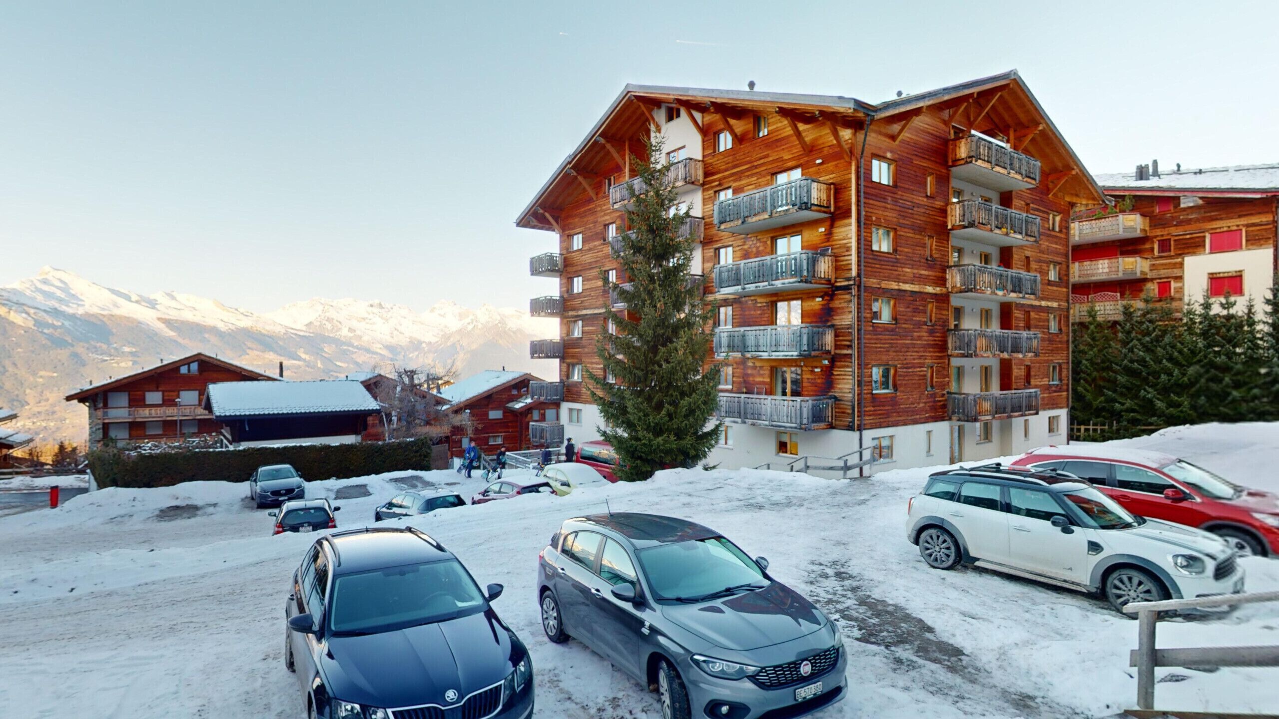 Un immeuble en bois à plusieurs étages, doté de balcons, entouré d’un sol enneigé et de voitures garées.