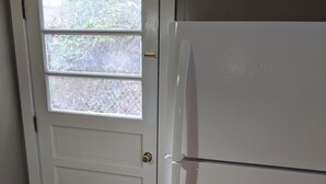 Una puerta blanca con ventanal, un refrigerador blanco y suelo de madera.
