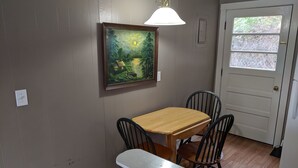 Un comedor con una mesa y sillas de madera, un cuadro en la pared y un ventanal con vistas a árboles.