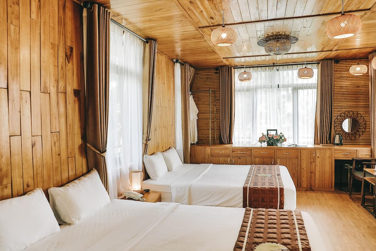 A hotel room with wooden walls and ceiling, two beds with white linens, a wooden desk, and a mirror.