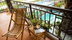 A wooden chair and a small table with a plant on a balcony with a view of a swimming pool. - Tam Coc Dibi Villa (Nam Hoa Lu)