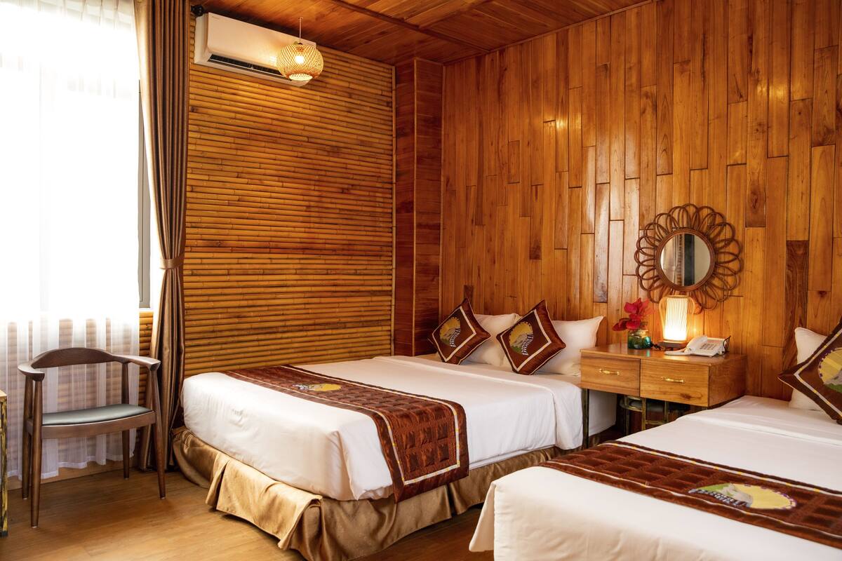 A hotel room with two beds, wooden paneling, a wooden nightstand, a chair, and a window with curtains.