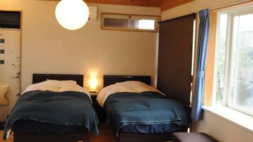 A room with two beds, a wooden ceiling, a table, and a window with curtains.