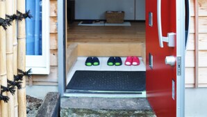 A red door leading into a room with a wooden floor, a white paper lantern, and a pair of shoes on a mat.