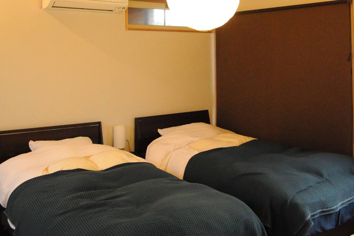 A bedroom with two beds, wooden beams, a ceiling light, and an air conditioning unit.