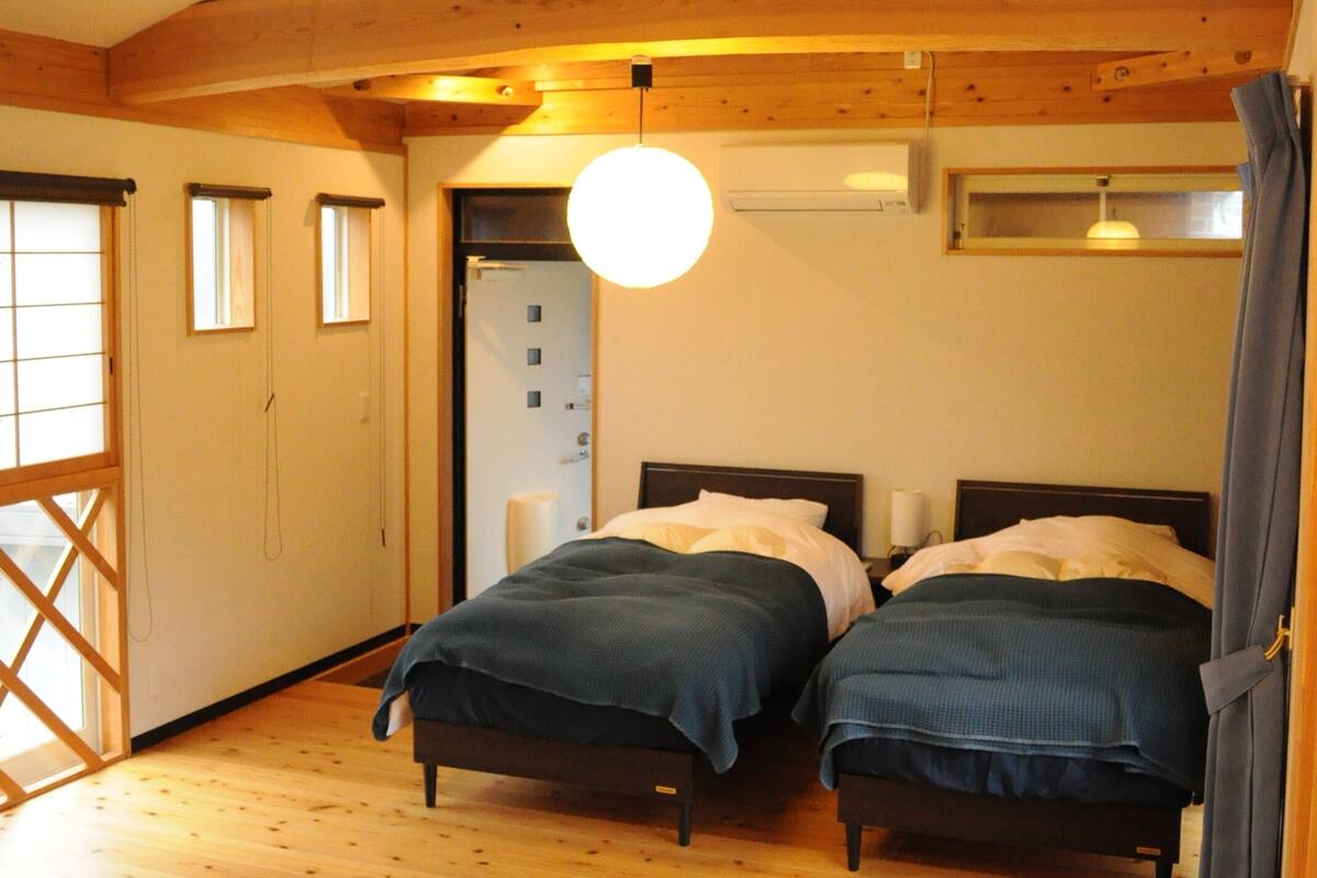 A wooden cabin bedroom with two beds, a small table, and a window with a view.