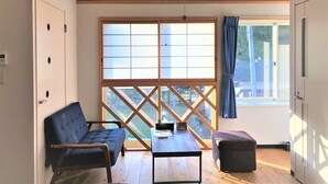 A room with a wooden ceiling, a large window with a view, a sofa, a table, and a chair.