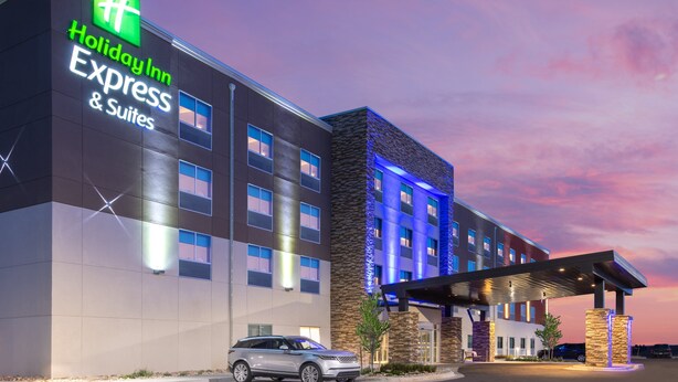 Un hotel Holiday Inn Express & Suites con un exterior moderno, una entrada cubierta y un estacionamiento.