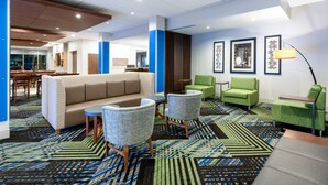 Un moderno vestíbulo de hotel con un sofá, sillas, una alfombra estampada y obras de arte enmarcadas en las paredes.