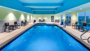Una piscina con sillas y tumbonas, rodeada de muros con amplias ventanas.
