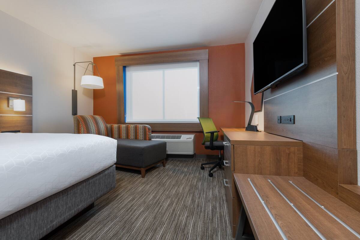 A hotel room with a bed, a desk, a chair, a TV, and a window.