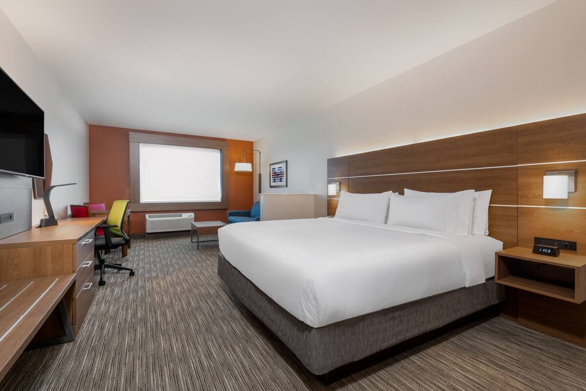A hotel room with a large bed, a desk with a chair, a TV, and a window.