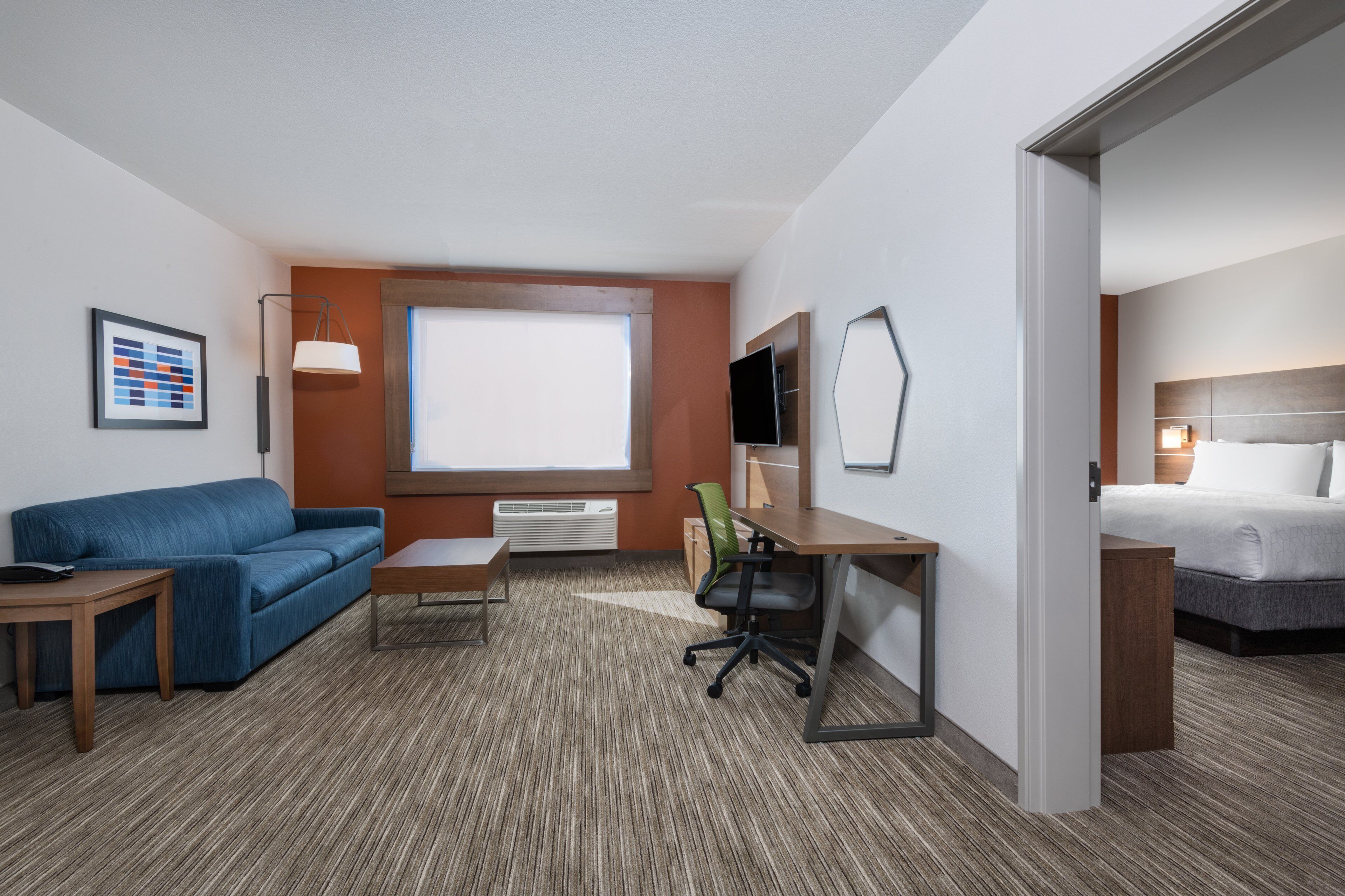 A hotel room with a blue sofa, a desk with a chair, a bed, a TV, and a window.