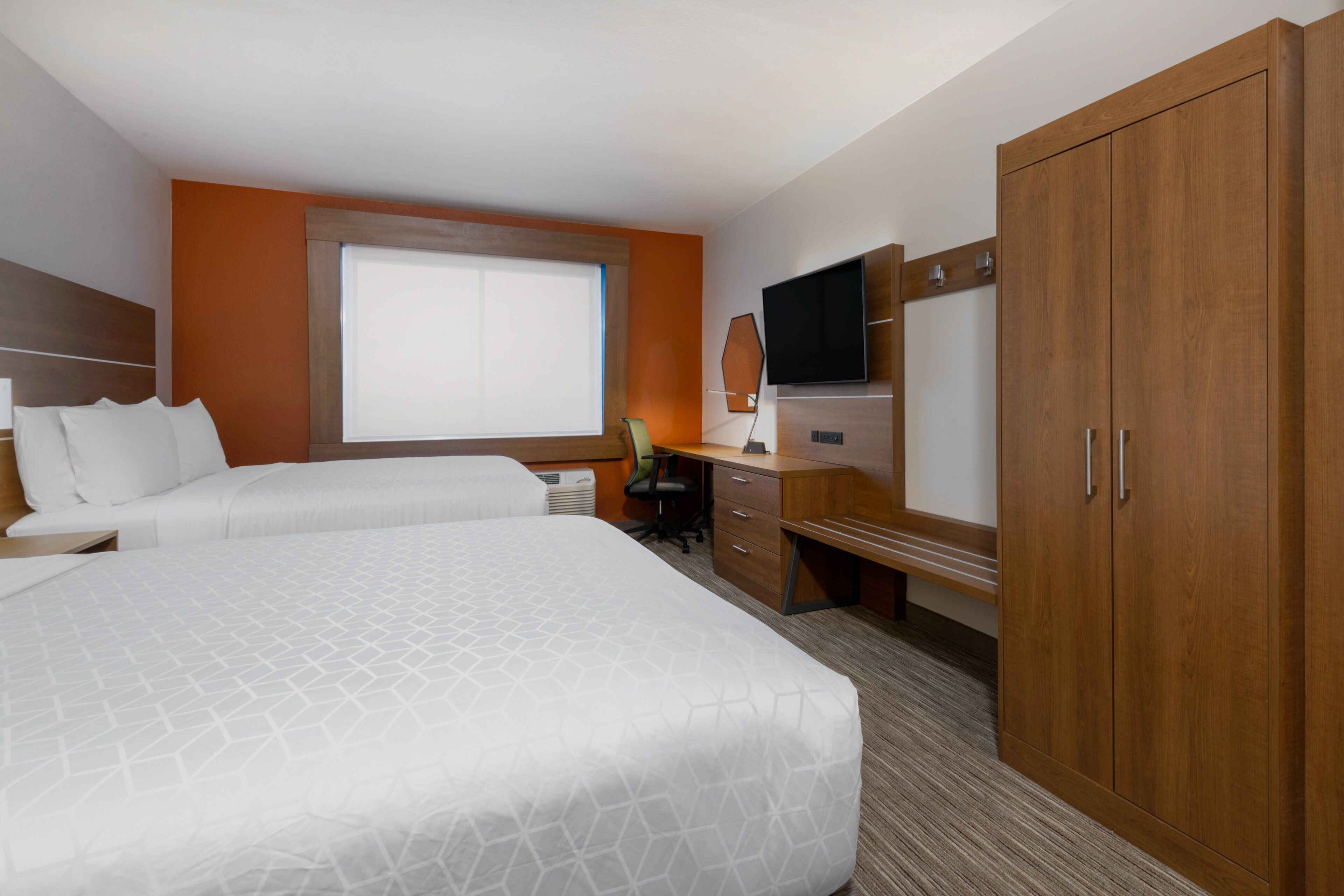 A hotel room with a large bed, a desk with a chair, a television, and a wardrobe.