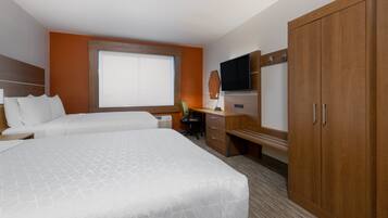 A hotel room with a large bed, a desk with a chair, a television, and a wardrobe.
