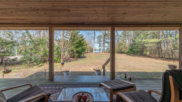 A covered deck with wooden chairs and a table, overlooking a forested area with a view of trees and a body of water. - Dock & Bay Access! Cabin on St. Jerome’s Creek (Ridge)