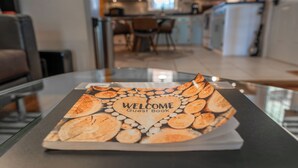 A welcome guest book on a glass table in a modern kitchen with a view of the dining area. - Dock & Bay Access! Cabin on St. Jerome’s Creek (Ridge)