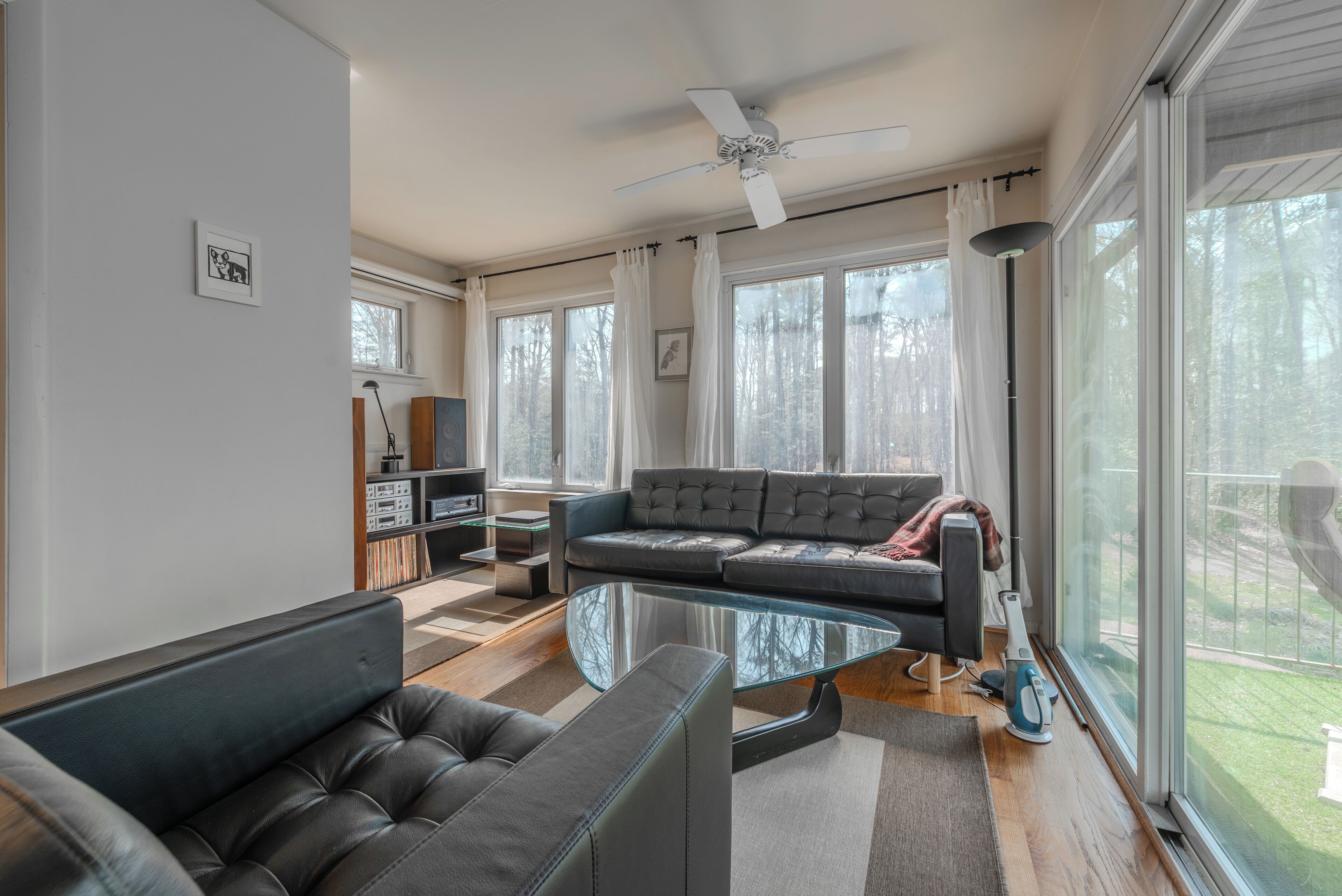 Ein modernes Wohnzimmer mit einer Couch, einem Glastisch, einem Deckenventilator und großen Fenstern.