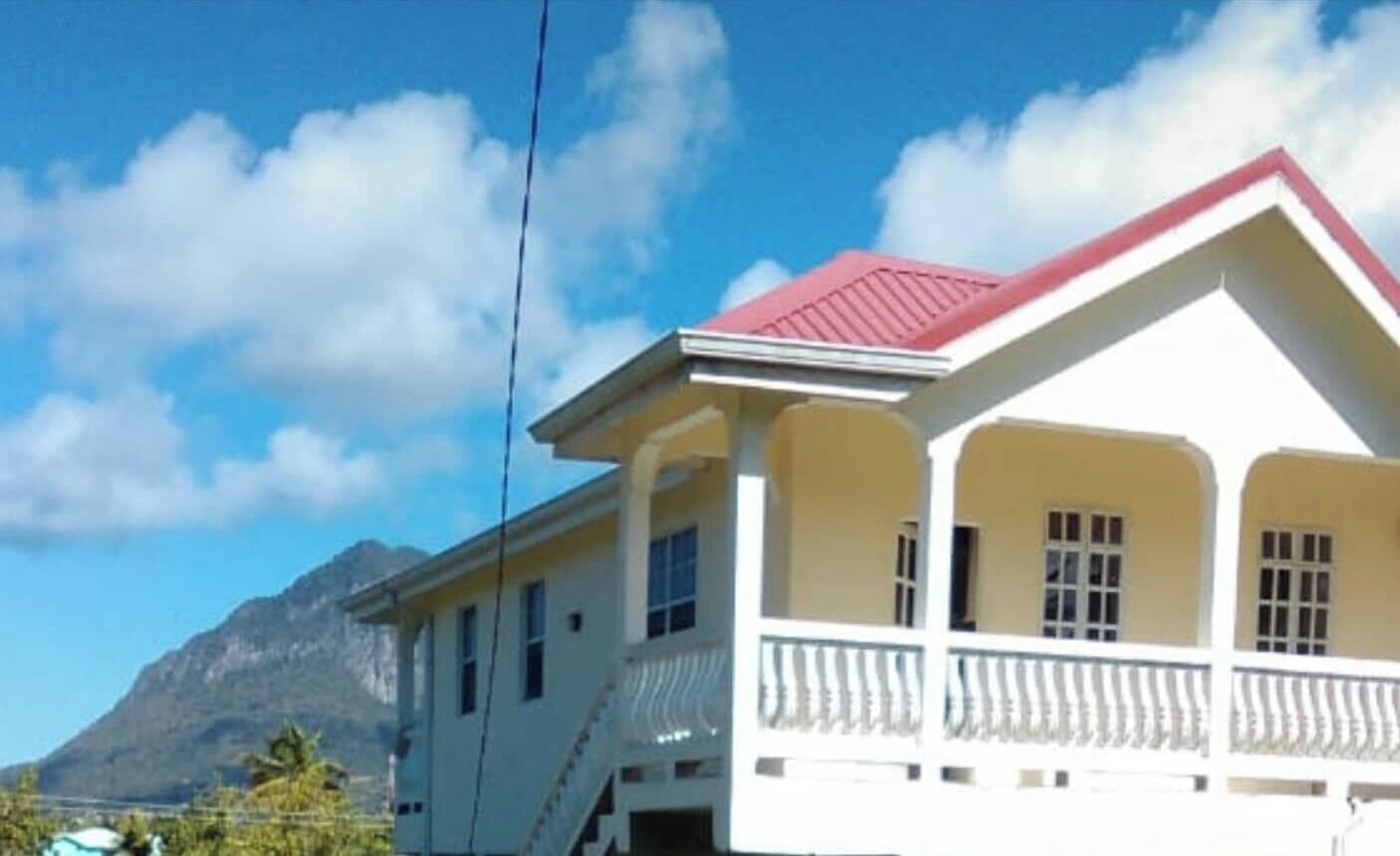 A two-story building with a red roof and white walls, featuring a balcony with white railings.