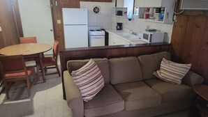 A cozy living area with a sofa and chairs, a small dining table, and a kitchen in the background. - Stand alone cabin,  sanitized, full kitchen. (Cadiz)