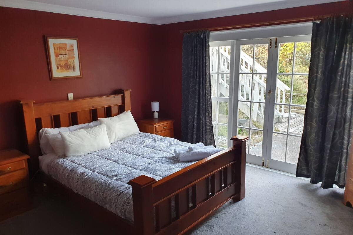 A bedroom with a wooden bed, a nightstand, a lamp, and a window with curtains.