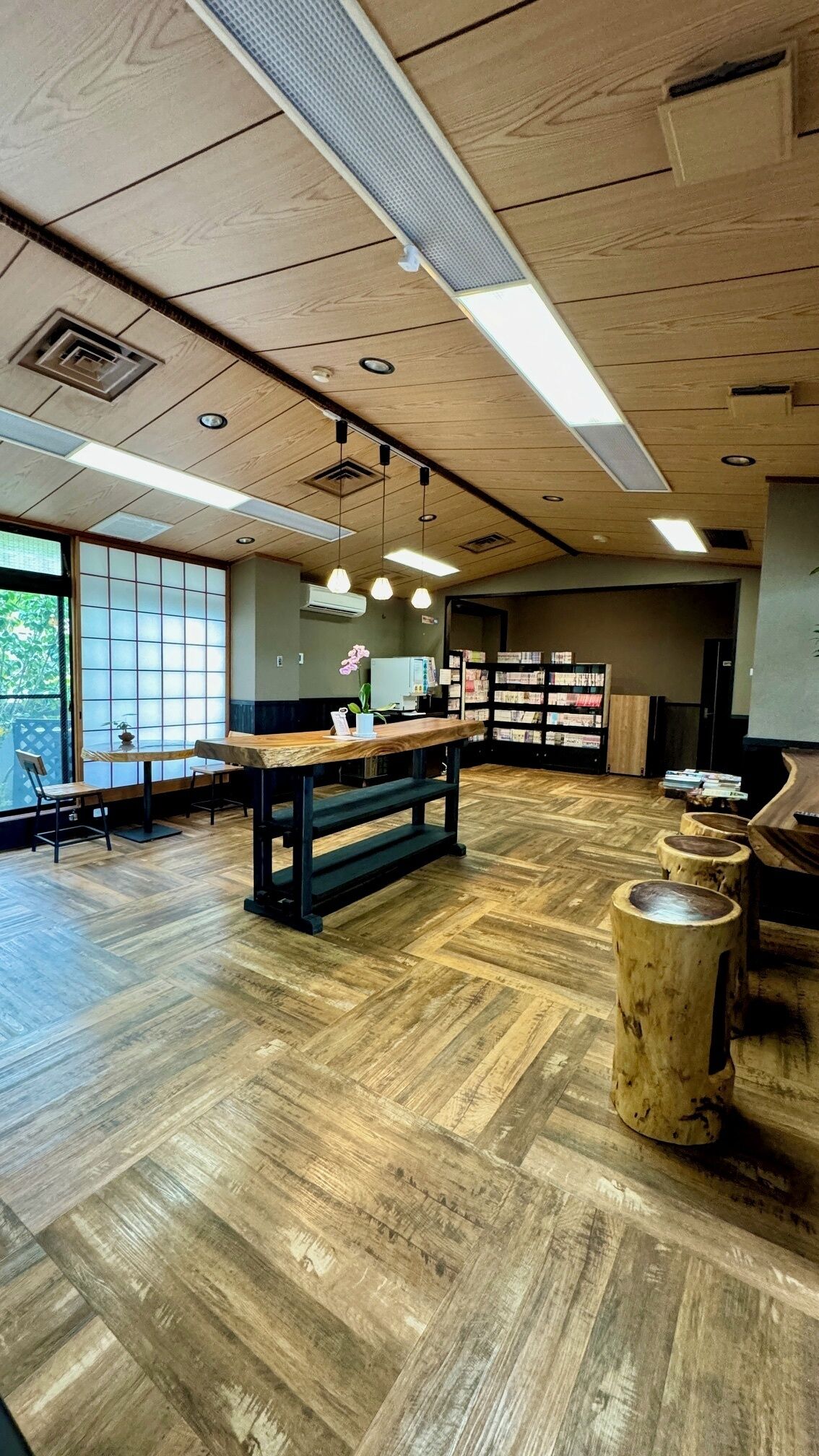 Une pièce spacieuse avec un plancher en bois, une table centrale entourée de chaises et une bibliothèque remplie de livres.