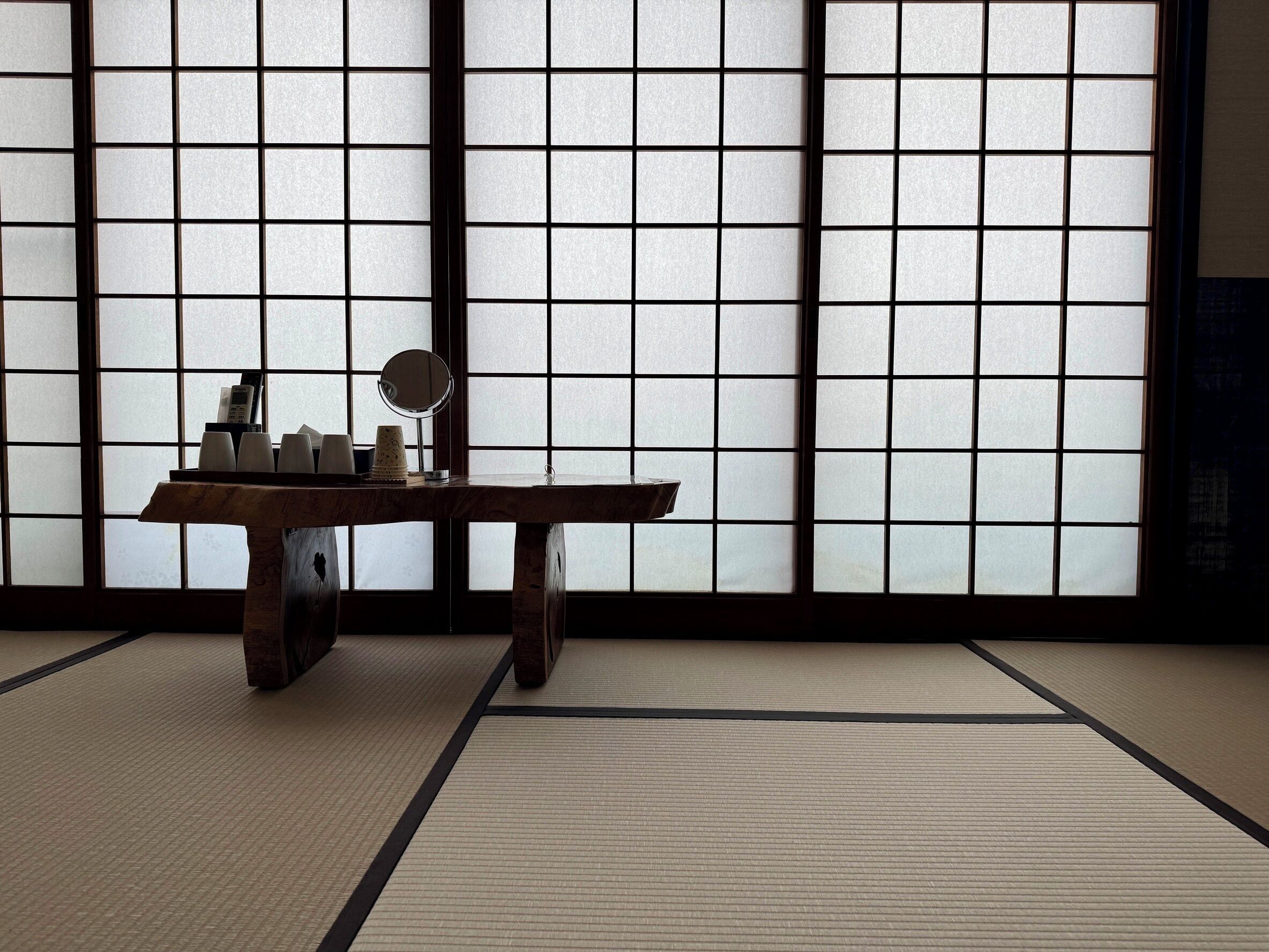 Una habitación con esteras de tatami, una mesa de madera baja y un espejo redondo, con algunos objetos sobre la mesa.