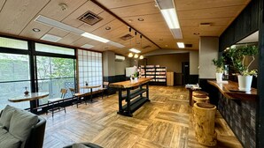 Un café chaleureux avec un plancher en bois, une table centrale, des chaises, une bibliothèque et de grandes fenêtres.