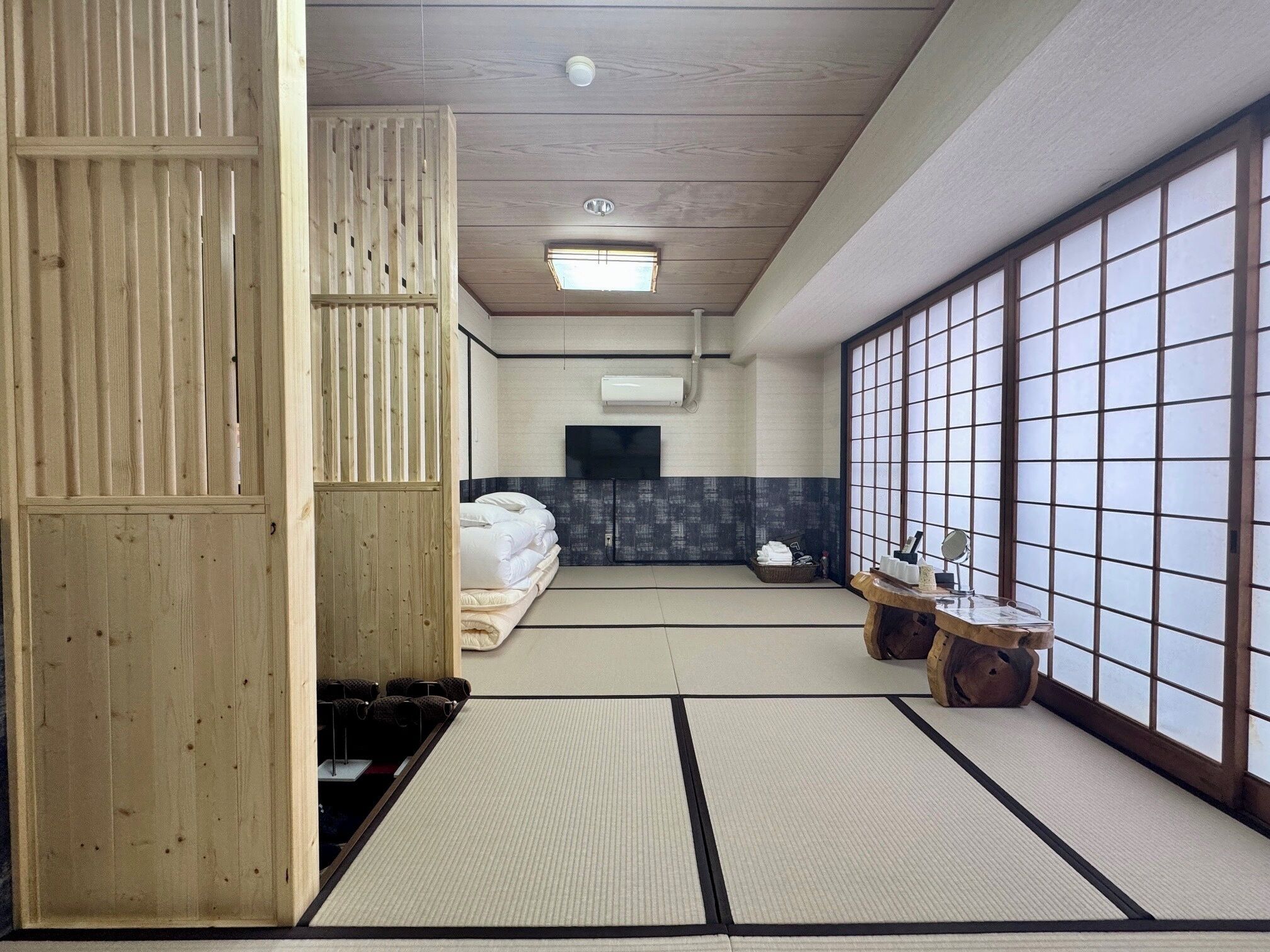 Habitació japonesa tradicional amb sòls de tatami, un llit de futó, una televisió i una porta corredissa amb un disseny de rejilla.