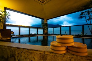 Zona de piscina con amplias ventanas, una silla de descanso y taburetes de madera.