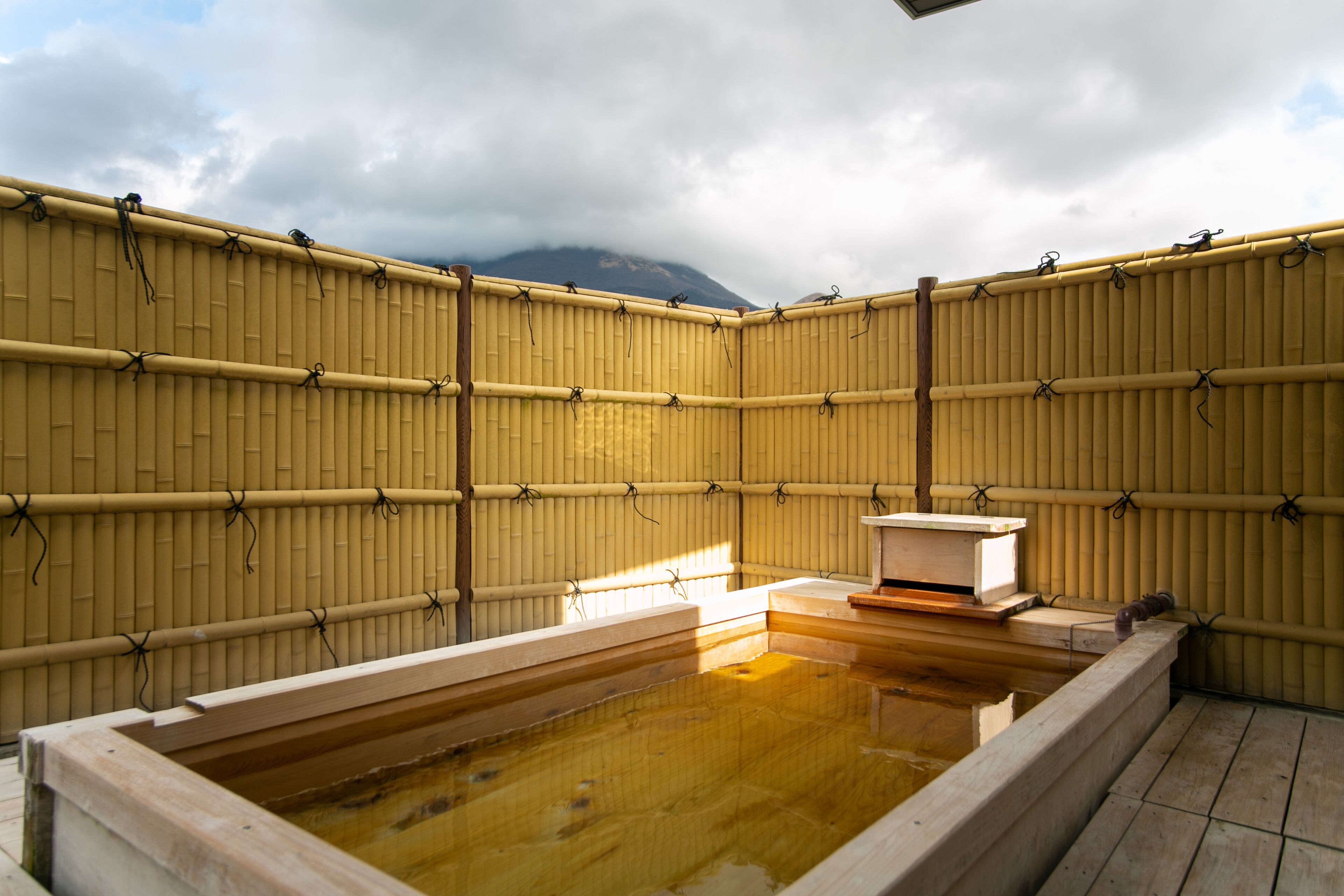 A traditional Japanese onsen with a wooden bath, bamboo walls, and a view of a mountain.