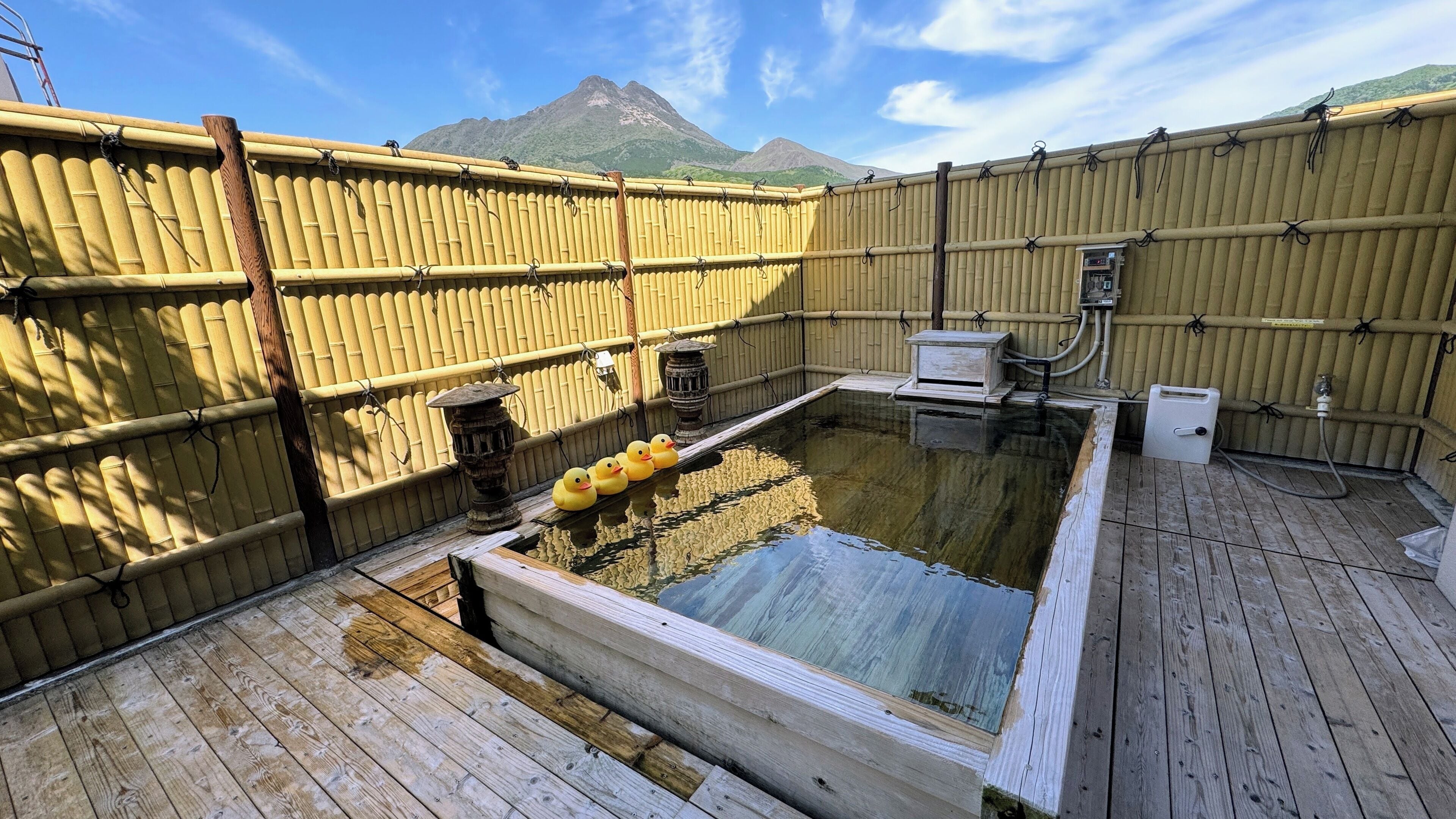 A traditional Japanese onsen with wooden flooring, a bamboo wall, and a hot spring bath.