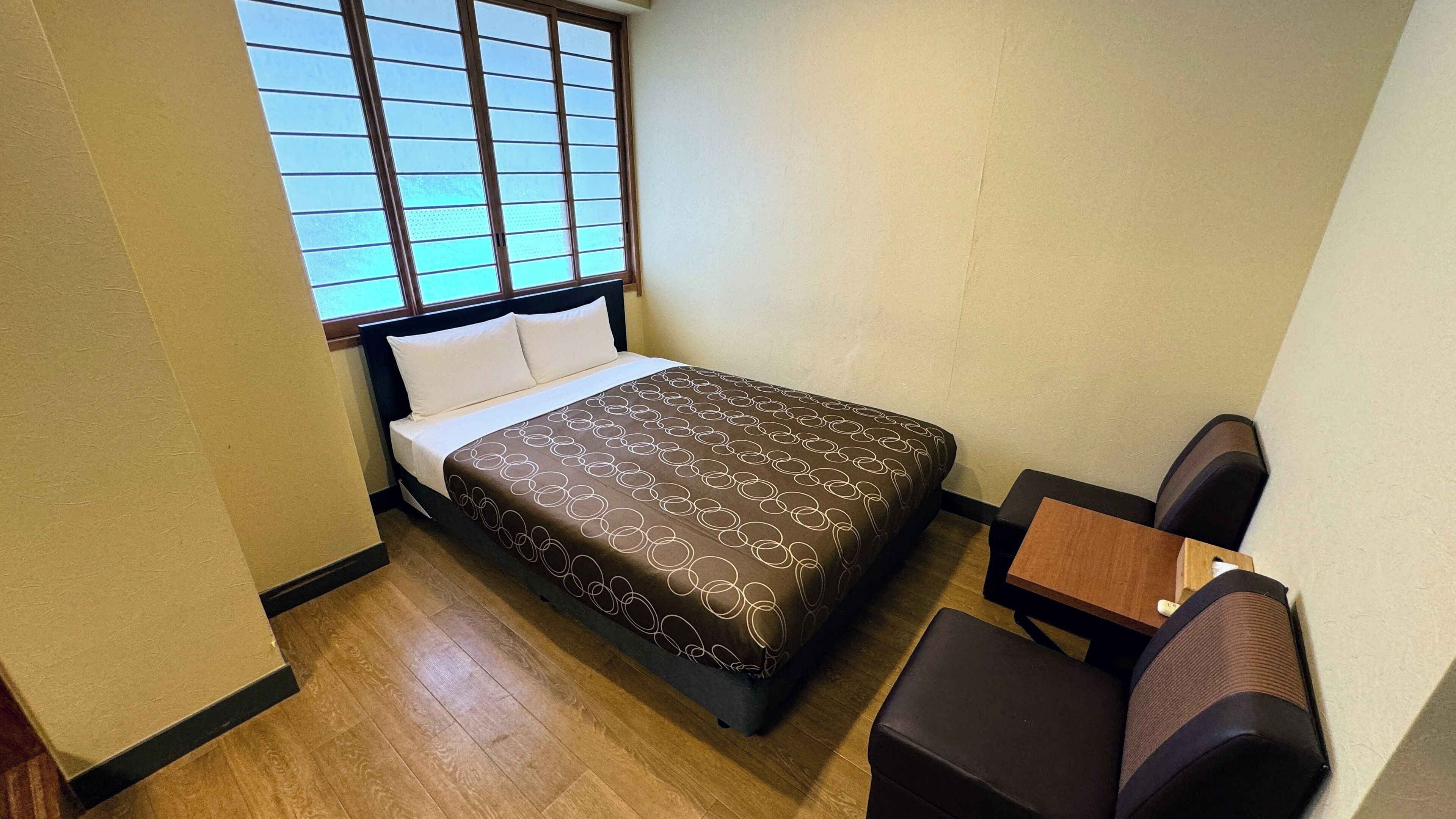 A small, neatly arranged hotel room with a bed, a small table, and a chair.