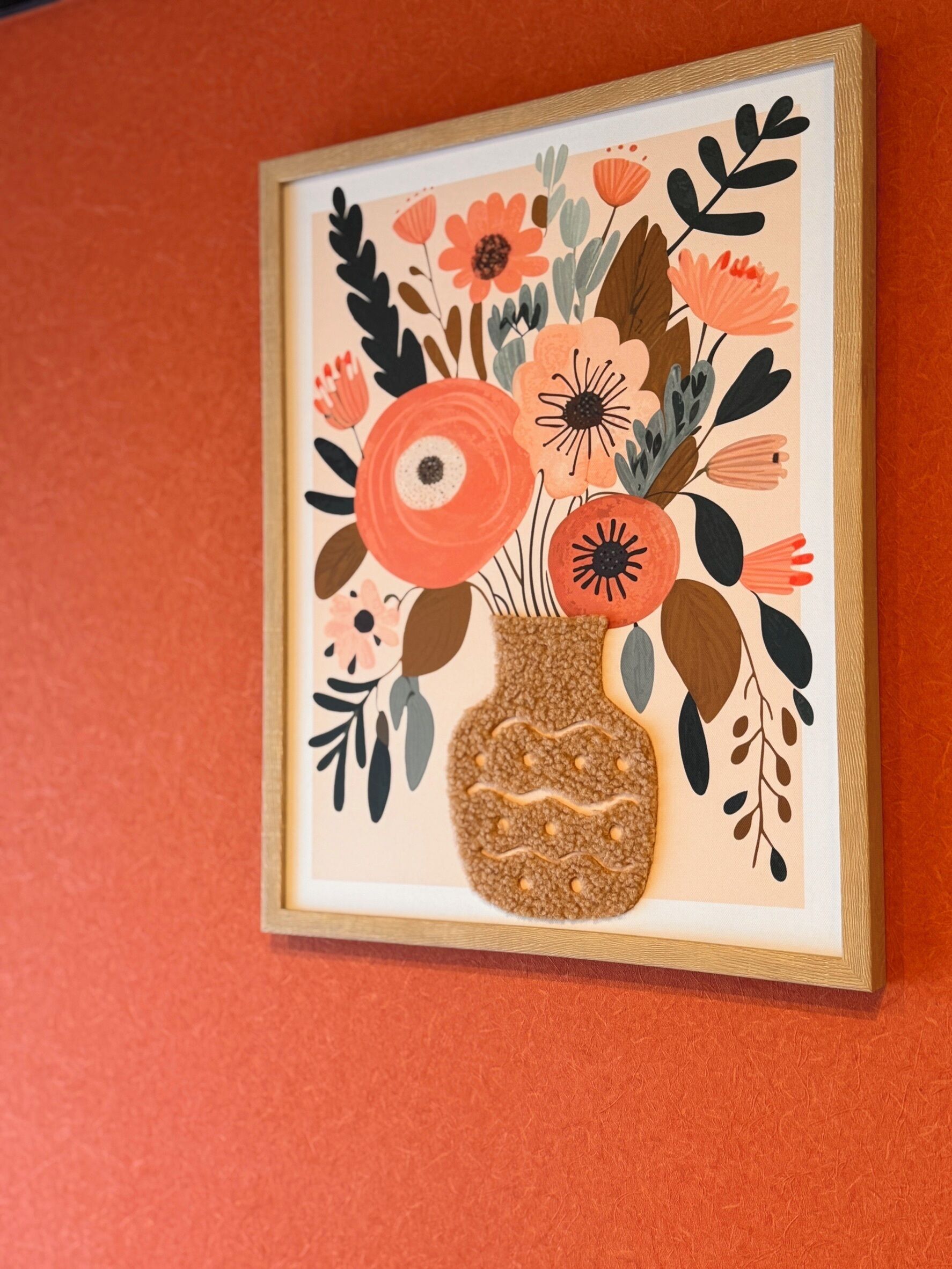 A framed artwork of a vase with flowers and leaves.