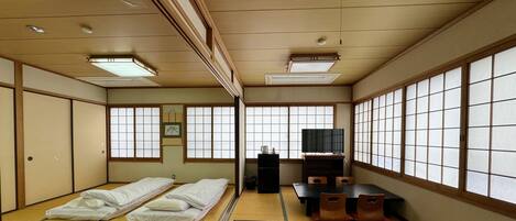 A traditional Japanese room with tatami flooring, a futon bed, a TV, and sliding doors.