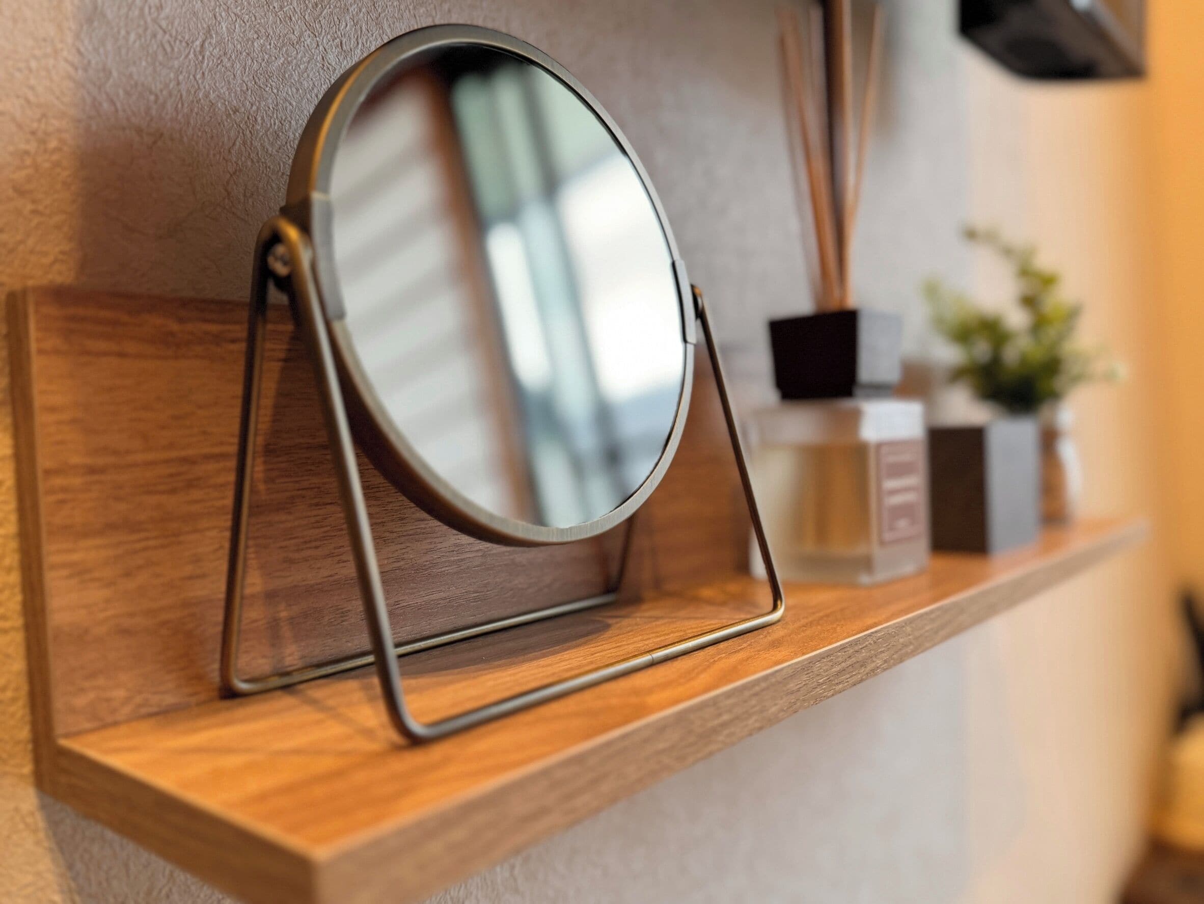 A wooden shelf with a round mirror and a small black object, possibly a speaker, on a wall.