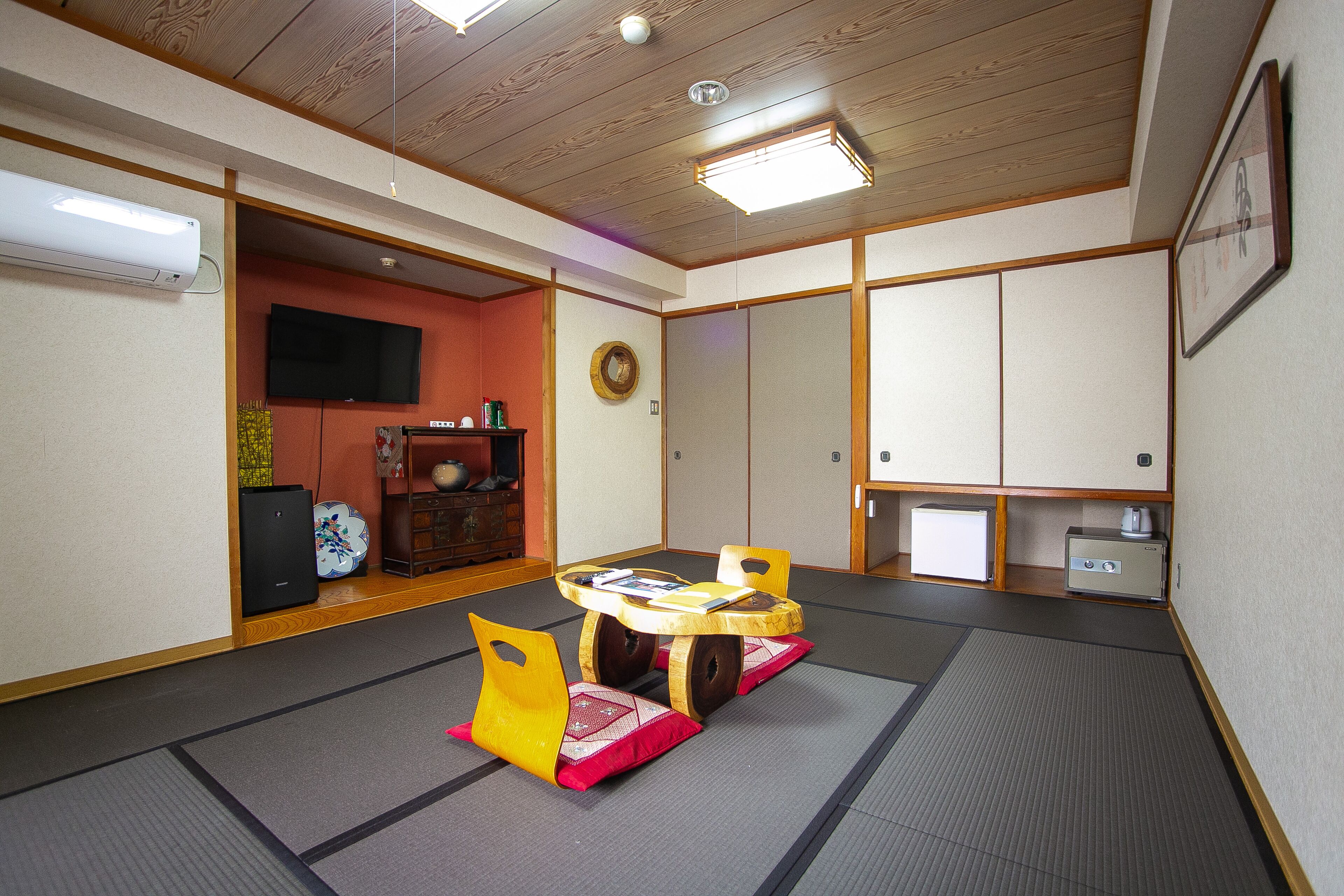 A traditional Japanese room with tatami flooring, a low wooden table, and a television mounted on the wall.