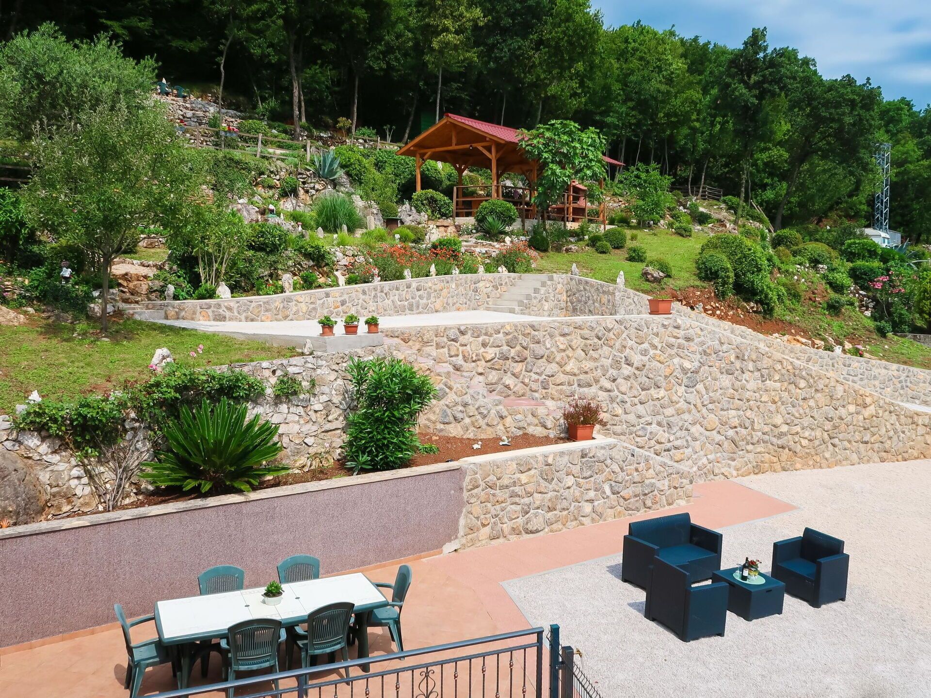 Un patio con escalones de piedra, mobiliario exterior y una estructura de madera al fondo.