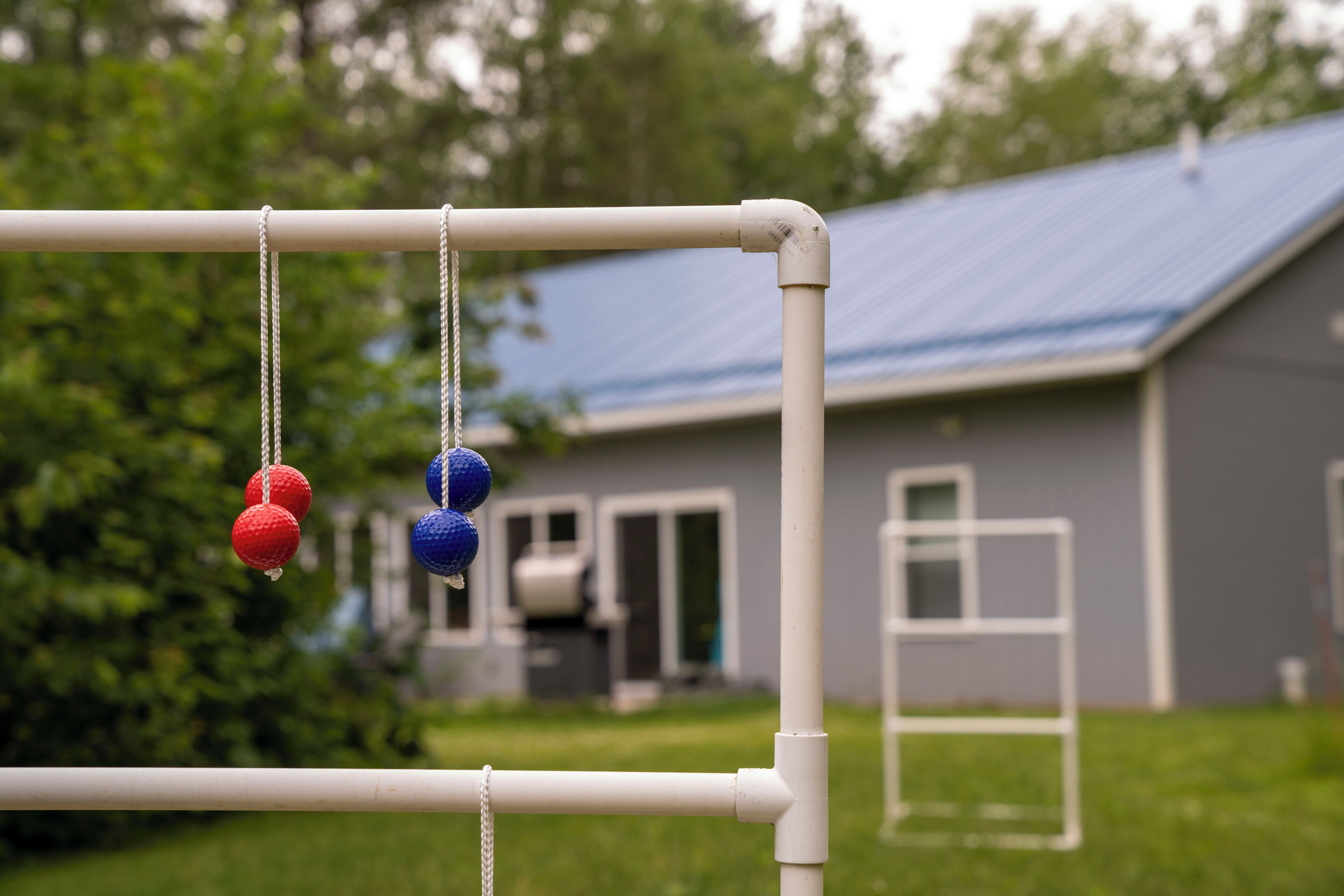 Una estructura metálica blanca con esferas rojas y azules colgando, frente a una casa con techo azul.