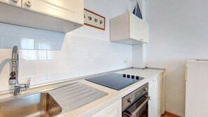 A modern kitchen with white cabinets, a stainless steel sink, a built-in oven, and a black induction cooktop.