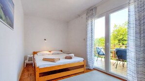 A bedroom with a wooden bed, a nightstand, a small table, and a window with curtains.