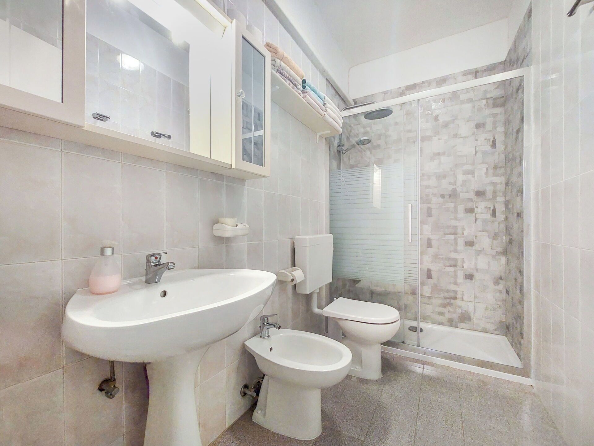 Een badkamer met een wastafel, twee toiletten en een douchecabine van glas.