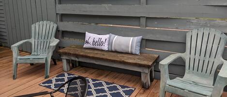 A wooden deck with two Adirondack chairs, a bench, and a patterned rug.