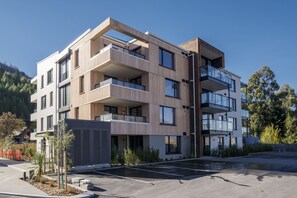 A multi-story modern building with balconies, large windows, and a parking area.