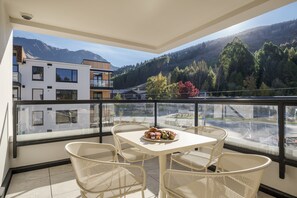 A balcony with a table set for two, overlooking a mountainous landscape.